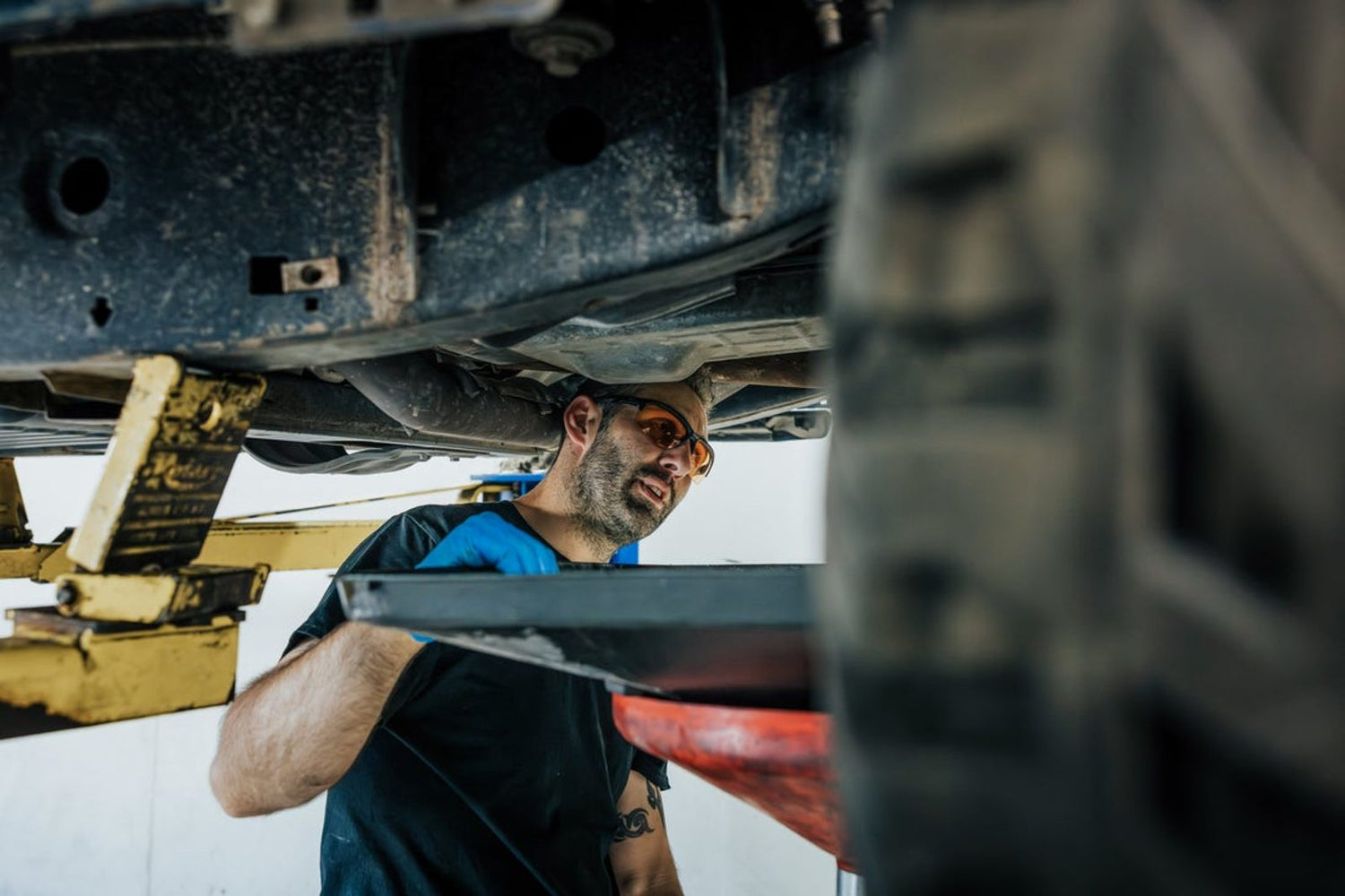 Auto technician in Z87 safety glasses working under a vehicle in a service bay